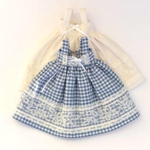 Könnte beinhalten: Ein blaues und weißes Gingham-Kleid mit weißer Spitzenborte und weißen Trägern. Das Kleid hat ein weißes Band, das in der Taille gebunden ist.