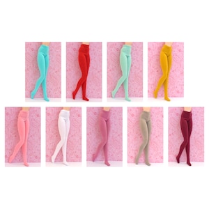 Può includere: Dieci paia di collant per bambole in vari colori, tra cui rosa, rosso, bianco, giallo e verde. I collant sono esposti su uno sfondo rosa.