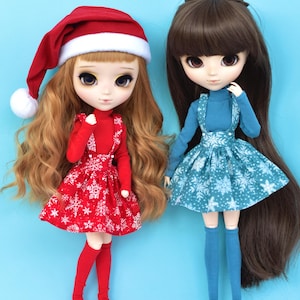 Può includere: Due bambole con abiti invernali. La bambola a sinistra indossa un cappello da Babbo Natale rosso, un maglione rosso, un vestito con stampa a fiocco di neve rosso e bianco e collant rossi. La bambola a destra indossa un maglione blu, un vestito con stampa a fiocco di neve blu e bianco e collant blu.