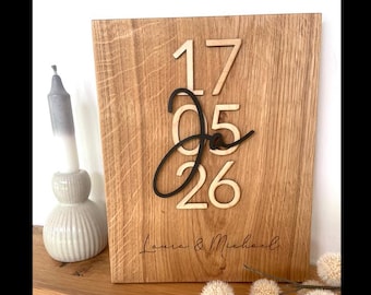 Puede incluir: Una placa de madera con los números "17 05 26" y los nombres "Laura & Michael" grabados. Los números son de color madera clara, con el "05" en escritura negra. La placa es de madera marrón claro.