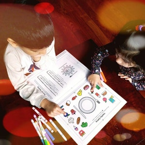 Op de afbeelding: Twee kinderen werken aan een kleurplaat met een afbeelding van een bord met gezond eten. De pagina heeft de titel "Gezond eten" en de tekst "Hou je van eten?" De kinderen gebruiken kleurpotloden om de afbeelding in te kleuren.