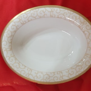 Peut inclure: Bol ovale blanc avec un bord doré et un motif de volutes dorées complexes.