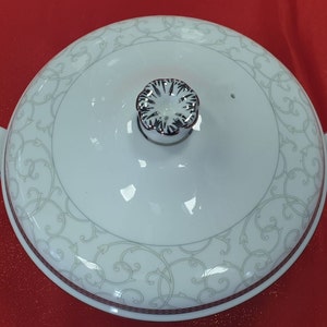 May include: White porcelain serving dish with a lid. The lid has a silver knob and a delicate floral pattern. The dish has a silver rim and a similar floral pattern.
