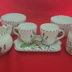 May include: A white ceramic tea set with lavender floral designs. The set includes a teapot, creamer, sugar bowl, and two teacups with saucers.