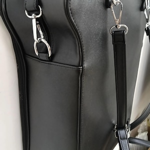 May include: Black satchel bag with silver-tone hardware. The bag features a structured design with a top handle and a detachable shoulder strap. The bag has a zippered closure and an exterior pocket.