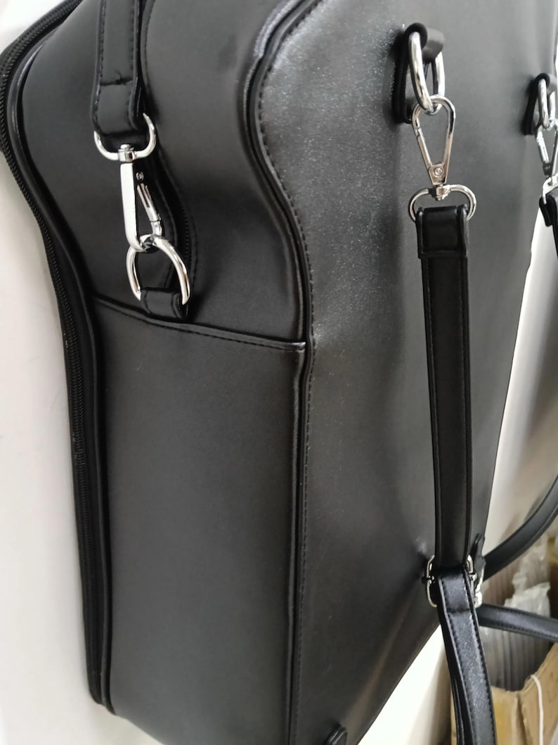 May include: Black satchel bag with silver-tone hardware. The bag features a structured design with a top handle and a detachable shoulder strap. The bag has a zippered closure and an exterior pocket.
