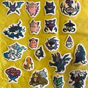 Puede incluir: Una colecci&oacute;n de veinte pegatinas troqueladas individuales que presentan varias criaturas de dibujos animados coloridas, incluyendo Gengar, Charmander y Clefairy, dispuestas sobre un fondo amarillo brillante. Cada pegatina tiene un dise&ntilde;o.