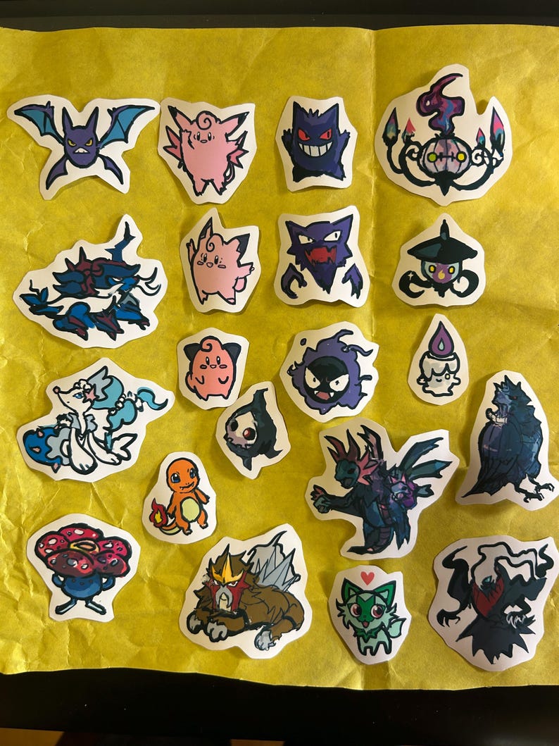 Puede incluir: Una colecci&oacute;n de veinte pegatinas troqueladas individuales que presentan varias criaturas de dibujos animados coloridas, incluyendo Gengar, Charmander y Clefairy, dispuestas sobre un fondo amarillo brillante. Cada pegatina tiene un dise&ntilde;o.