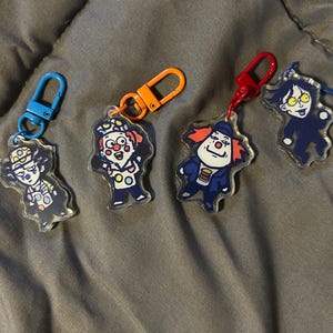 May include: Four colourful keychains featuring cartoon characters. Each keychain has a different character with a unique design and colour scheme. The keychains are made of clear acrylic and have metal rings for attaching to keys or bags.