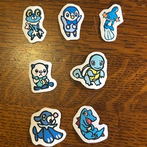 Puede incluir: Una colecci&oacute;n de siete pegatinas de papel individuales con ilustraciones dibujadas a mano de varias criaturas de dibujos animados en tonos azules. Cada pegatina tiene un borde blanco y representa un personaje &uacute;nico con expresiones faciales.