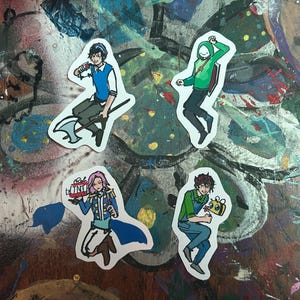 Peut inclure: Quatre autocollants de personnages de dessins anim&eacute;s color&eacute;s sur une surface peinte. Les autocollants repr&eacute;sentent un personnage avec un sweat &agrave; capuche vert, un personnage avec une chemise bleue et un gilet vert, un personnage avec un uniforme bleu et blanc, et un personnage avec une chemise verte et un jean bleu.