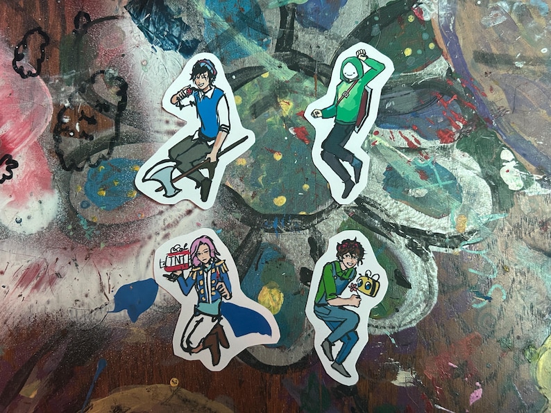 Peut inclure: Quatre autocollants de personnages de dessins anim&eacute;s color&eacute;s sur une surface peinte. Les autocollants repr&eacute;sentent un personnage avec un sweat &agrave; capuche vert, un personnage avec une chemise bleue et un gilet vert, un personnage avec un uniforme bleu et blanc, et un personnage avec une chemise verte et un jean bleu.