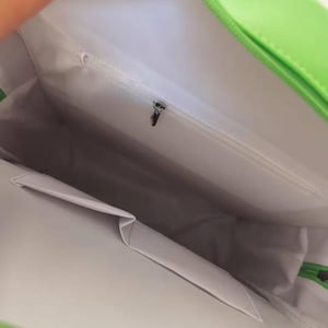 May include: Bright green handbag with a white interior. The bag has a zippered pocket and a small pocket on the inside. The bag is open, revealing the interior lining and pockets.