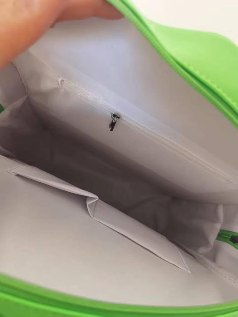 May include: Bright green handbag with a white interior. The bag has a zippered pocket and a small pocket on the inside. The bag is open, revealing the interior lining and pockets.