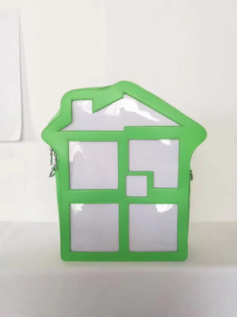 May include: A unique, house-shaped handbag with a bright green frame and clear, window-like panels. The bag features a zipper closure and a shoulder strap. The design is modern and playful, suitable for carrying essentials.