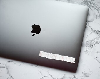 May include: A silver laptop computer with a black Apple logo on the lid. A white sticker with the text "Iced Coffee Please" is on the bottom right corner of the laptop.