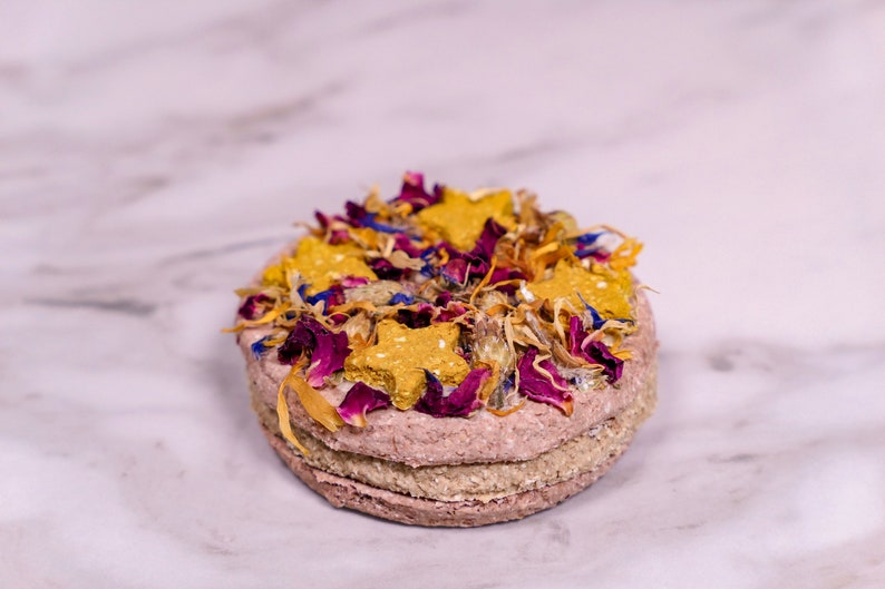 May include: A layered dog treat topped with dried flowers and star-shaped biscuits.
