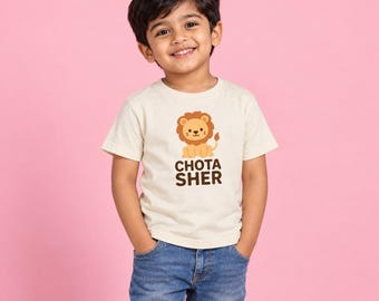 May include: A cream-colored short-sleeve t-shirt featuring a graphic of a cartoon lion and the text CHOTA SHER in brown letters, paired with blue denim jeans. The shirt has a crew neckline and a standard fit, showcasing a simple design.