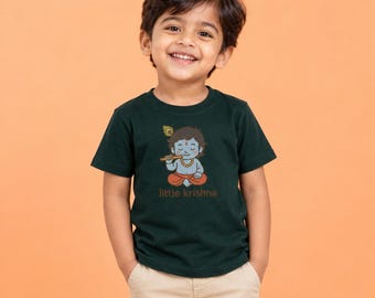 May include: A dark green short-sleeved t-shirt featuring a graphic of a blue-skinned child playing a flute, wearing orange pants and a peacock feather in their hair, with the text "little krishna" printed in brown below the graphic.