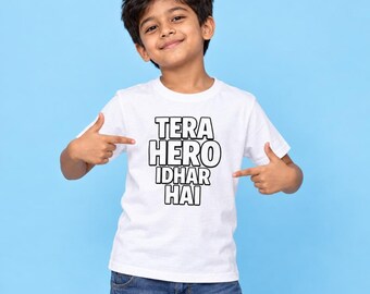 May include: A white short-sleeved t-shirt featuring the black text TERA HERO IDHAR HAI printed in a bold, blocky font on the chest. The garment is paired with blue denim jeans, creating a casual look with clear, legible lettering on the front.