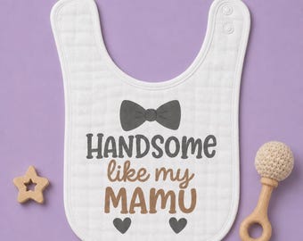 May include: A white fabric baby bib featuring a dark gray bow tie graphic above the text "HANDSOME like my MAMU" in dark gray and brown lettering, with two small dark gray heart icons at the bottom and two snap closures at the top neck strap.