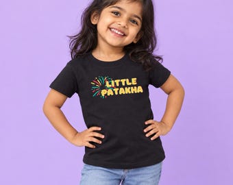 May include: A black short-sleeved t-shirt featuring a graphic of colorful fireworks and the yellow text "LITTLE PATAKHA" printed on the chest. The shirt is paired with light blue denim jeans, creating a casual look with a vibrant, festive design.
