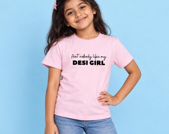 May include: A light pink short-sleeved t-shirt featuring the black text "Aint nobody like my DESI GIRL" printed on the chest, accented by small star graphics. The shirt has a crew neckline and a standard fit, constructed from a solid-colored fabric.