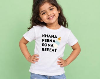 May include: A white short-sleeved t-shirt featuring the black text KHANA PEENA SONA REPEAT and a graphic of a baby bottle with a tan cap and light blue base. The shirt is paired with blue denim jeans decorated with small white flower patterns.