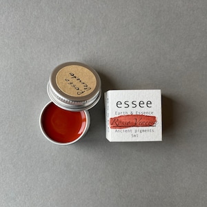 Pu&ograve; includere: Un piccolo barattolo di pigmento rosso etichettato "essee Earth & Essence Rosso Veneziano Ancient pigments 5ml". Il barattolo &egrave; aperto e il pigmento rosso &egrave; visibile all'interno.