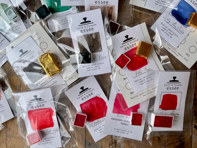 May include: An assortment of watercolour paint pans in various colours, including red, gold, and black. Each pan is labelled with the brand name "Earth & Essence essee" and a description of the colour. The pans are packaged in clear plastic bags.