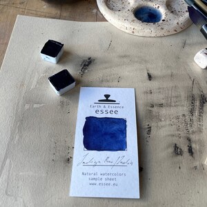 Op de afbeelding: Een monstersheet voor Indigo Blue aquarelverf van Earth & Essence essee. Het blad toont een klein vierkantje van de verf en de tekst "Indigo Blue/Indigo" in cursief.