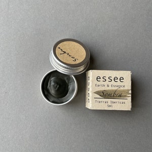 Pu&ograve; includere: Un piccolo barattolo d'argento di inchiostro nero con un'etichetta che recita "Sombra" e una scatola pi&ugrave; grande con il testo "essee Earth & Essence Sombra Tierras Ibericas 5ml".