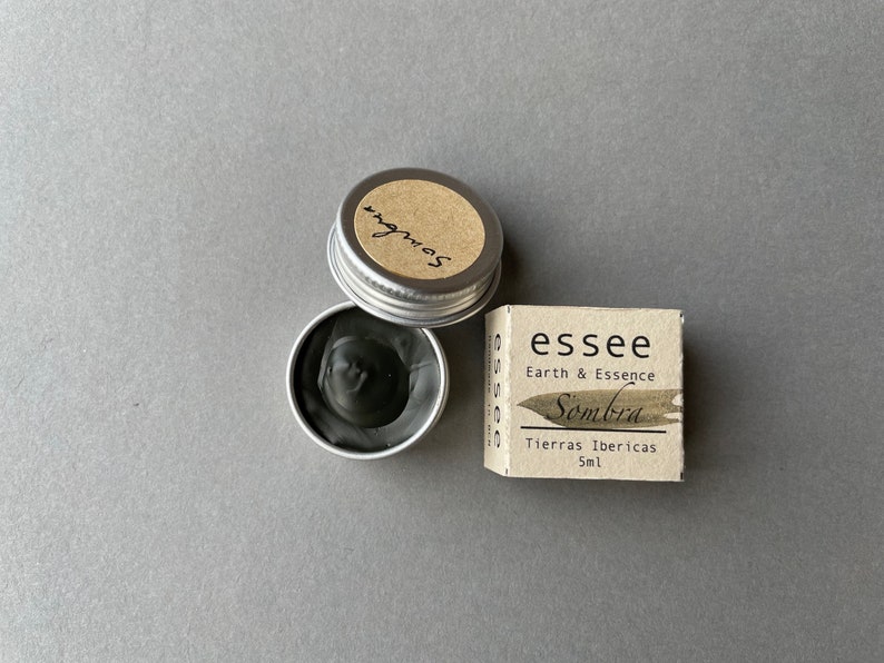 Pu&ograve; includere: Un piccolo barattolo d'argento di inchiostro nero con un'etichetta che recita "Sombra" e una scatola pi&ugrave; grande con il testo "essee Earth & Essence Sombra Tierras Ibericas 5ml".
