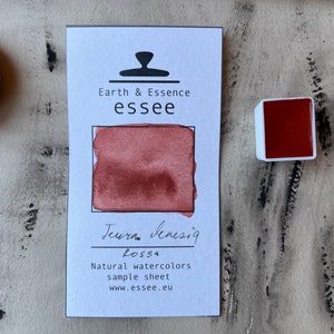 Puede incluir: Una muestra de pintura de acuarela con el texto "Earth & Essence essee" y "Terra Sensig Rossa" en tinta negra. La muestra muestra una muestra de pintura de acuarela de color rojo-marr&oacute;n.