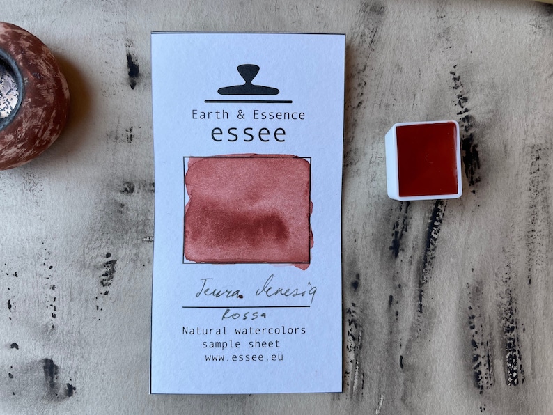 Puede incluir: Una muestra de pintura de acuarela con el texto "Earth & Essence essee" y "Terra Sensig Rossa" en tinta negra. La muestra muestra una muestra de pintura de acuarela de color rojo-marr&oacute;n.