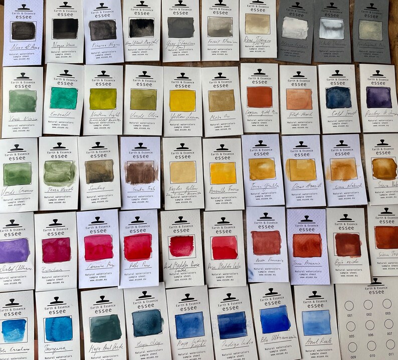 Puede incluir: Una colecci&oacute;n de 60 muestras de pintura acuarela en varios colores, dispuestas en filas sobre una superficie blanca. Cada muestra est&aacute; etiquetada con el nombre del color y la marca "essee".