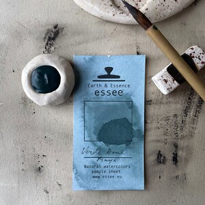 Op de afbeelding: Een monsterblad voor natuurlijke aquarelverf Verde Aqua Maya. Het blad is blauw met een donkergroene aquarelwas en de tekst "Earth & Essence essee" en "Verde Aqua Maya Natuurlijke aquarelverven monsterblad www.essee.eu".