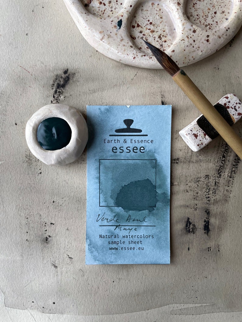 Op de afbeelding: Een monsterblad voor natuurlijke aquarelverf Verde Aqua Maya. Het blad is blauw met een donkergroene aquarelwas en de tekst "Earth & Essence essee" en "Verde Aqua Maya Natuurlijke aquarelverven monsterblad www.essee.eu".