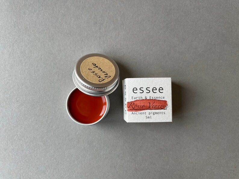 Pu&ograve; includere: Un piccolo barattolo di pigmento rosso etichettato "essee Earth & Essence Rosso Veneziano Ancient pigments 5ml". Il barattolo &egrave; aperto e il pigmento rosso &egrave; visibile all'interno.