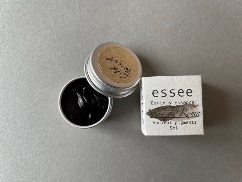 Pu&ograve; includere: Un piccolo contenitore argentato di pigmento nero etichettato "Nero di Roma" dal marchio "essee Earth & Essence". L'etichetta riporta anche "Pigmenti antichi 5ml".