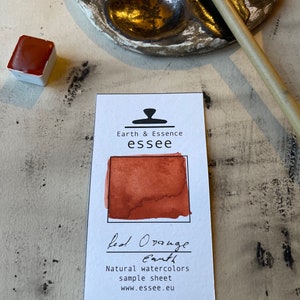 Puede incluir: Una hoja de muestra de pintura de acuarela Tierra naranja roja de la marca Earth & Essence essee. La pintura es de un color naranja-rojo vibrante. La hoja incluye el nombre de la marca, el sitio web y el texto "Muestra de acuarelas naturales".