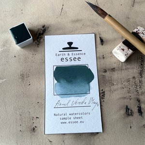 Op de afbeelding: Een aquarelverf-staalkaart met de tekst "Earth & Essence essee" en "Azul Verde Maya". De kaart toont een staal van de aquarelverf in een blauwgroene kleur.