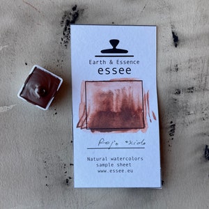 Puede incluir: Una peque&ntilde;a bandeja de pintura de acuarela rojo-marr&oacute;n con una muestra del color pintada en una tarjeta blanca. La tarjeta tiene el texto "Earth & Essence essee" y "Rojo oxido" escrito en ella. La tarjeta tambi&eacute;n incluye el texto "Natural watercolors sample sheet www.essee.eu".