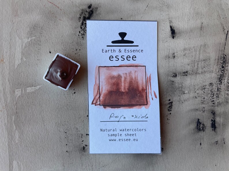 Puede incluir: Una peque&ntilde;a bandeja de pintura de acuarela rojo-marr&oacute;n con una muestra del color pintada en una tarjeta blanca. La tarjeta tiene el texto "Earth & Essence essee" y "Rojo oxido" escrito en ella. La tarjeta tambi&eacute;n incluye el texto "Natural watercolors sample sheet www.essee.eu".