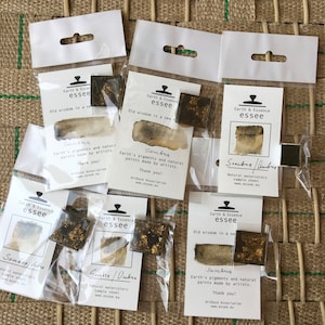 May include: Six small sample watercolour paint squares in clear plastic packaging. Each square is labelled "Sombra" and features a different shade of brown with gold flecks. The packaging includes the brand name "Earth & Essence essee" and the text "Old wisdom in a new way".