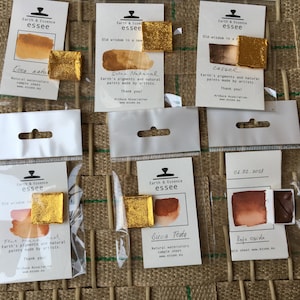 May include: Six small watercolour paint pans in individual plastic packaging. The pans are labelled with the brand name "Earth & Essence essee" and the names of the colours: "Cua natu", "Selen Natural", "Cassel", "Flat", "Birua Tota", and "Rojo Ocre".