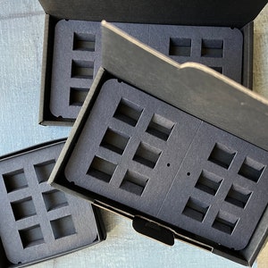 Puede incluir: Tres cajas negras con insertos de espuma para guardar objetos peque&ntilde;os. Las cajas est&aacute;n abiertas y los insertos de espuma son visibles. Los insertos de espuma tienen m&uacute;ltiples recortes rectangulares.