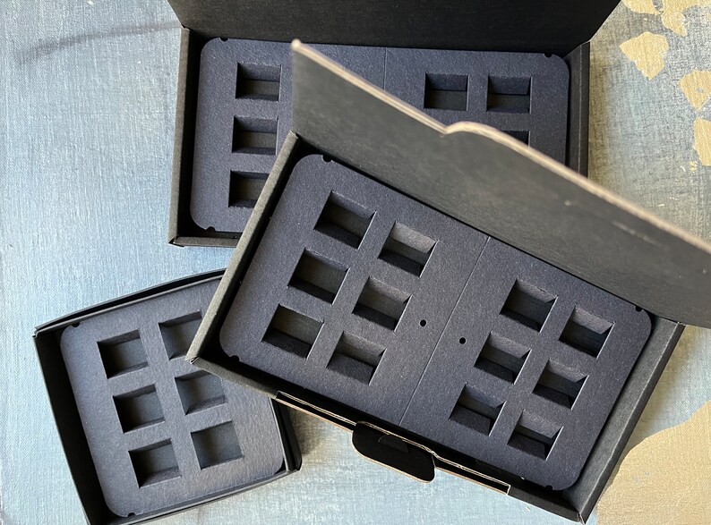 Puede incluir: Tres cajas negras con insertos de espuma para guardar objetos peque&ntilde;os. Las cajas est&aacute;n abiertas y los insertos de espuma son visibles. Los insertos de espuma tienen m&uacute;ltiples recortes rectangulares.