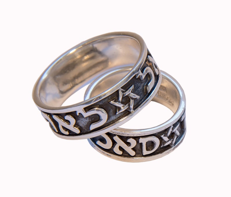 May include: Two silver rings with Hebrew writing and a Star of David. The rings are intertwined.
