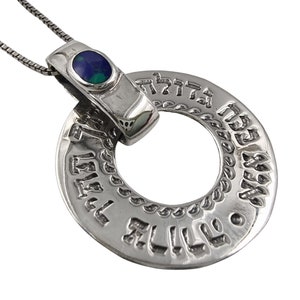 Puede incluir: Collar con colgante de plata con un diseño circular con texto hebreo. El colgante tiene una pequeña piedra ovalada con tonos azules y verdes. La cadena del collar es una fina cadena de plata.
